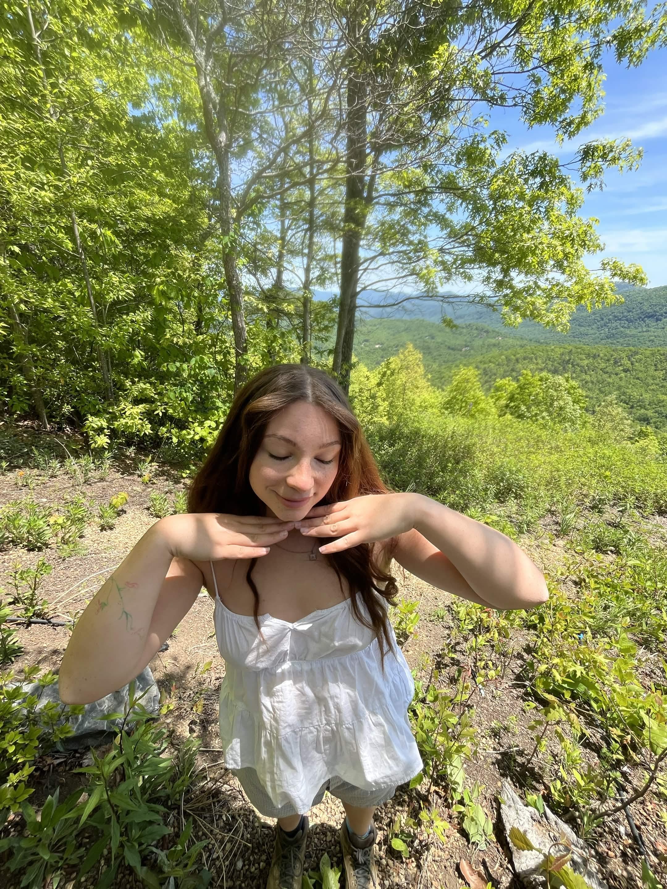 Kay outdoors with hands under chin, mountain backdrop